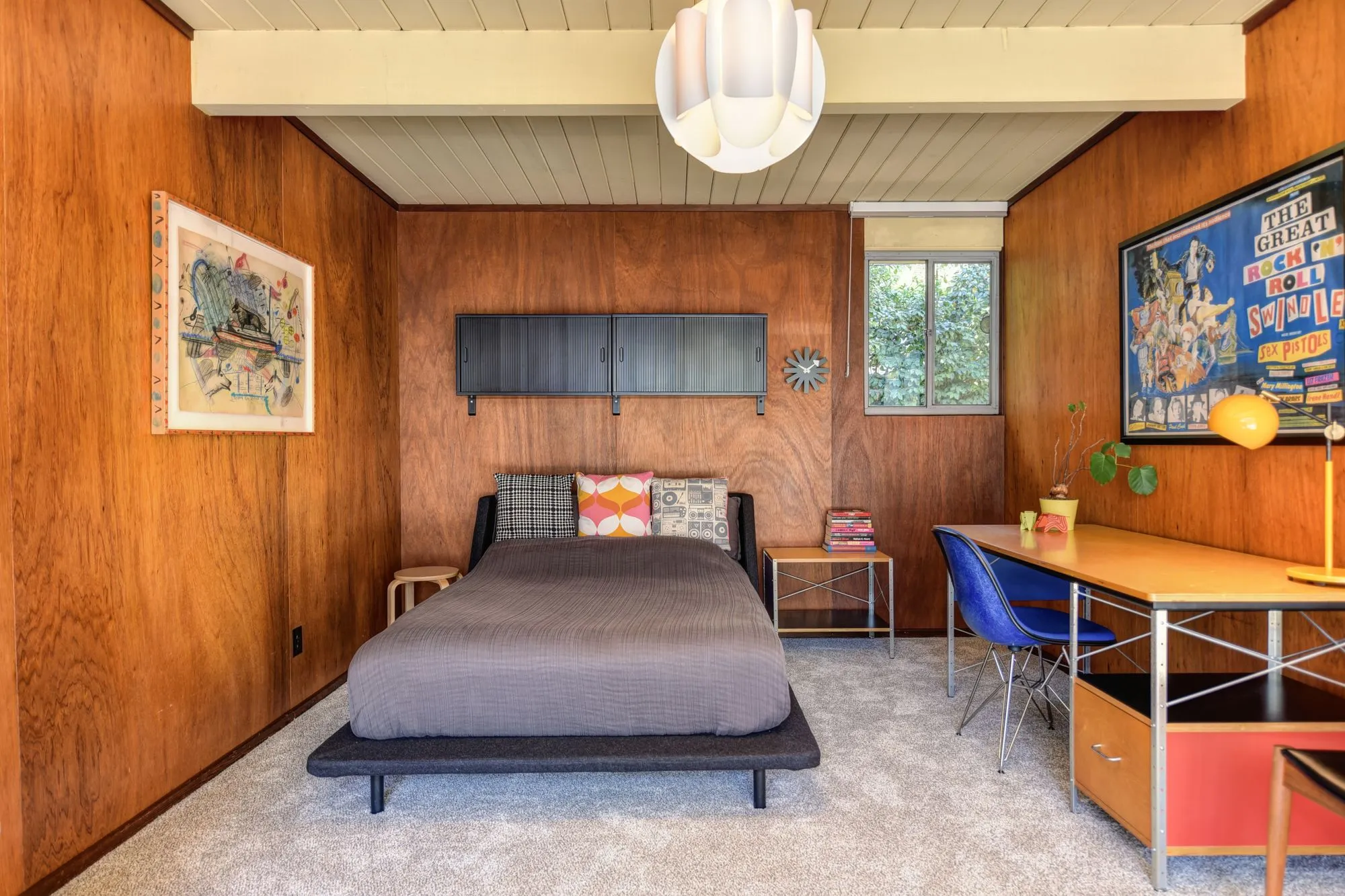 Bedroom with walnut-paneled walls, a low bed and a desk under the window